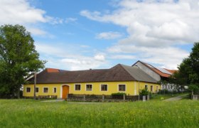 Gelbes Bauernhaus auf einer gr&uuml;nen Wiese mit blauem Himmel und Wolken.