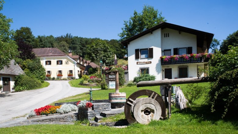 Ein l&auml;ndliches G&auml;stehaus mit Blumen und einem alten M&uuml;hlstein im Vordergrund.