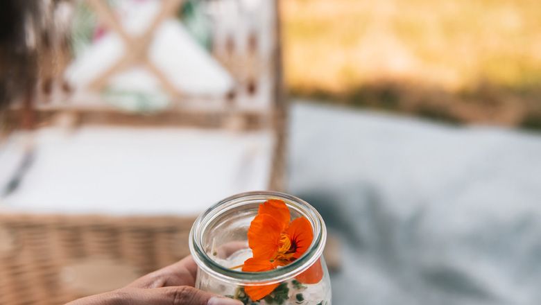 Nahaufnahme eines Dessertglases mit einer orangefarbenen Blume, im Hintergrund ein Picknickkorb.