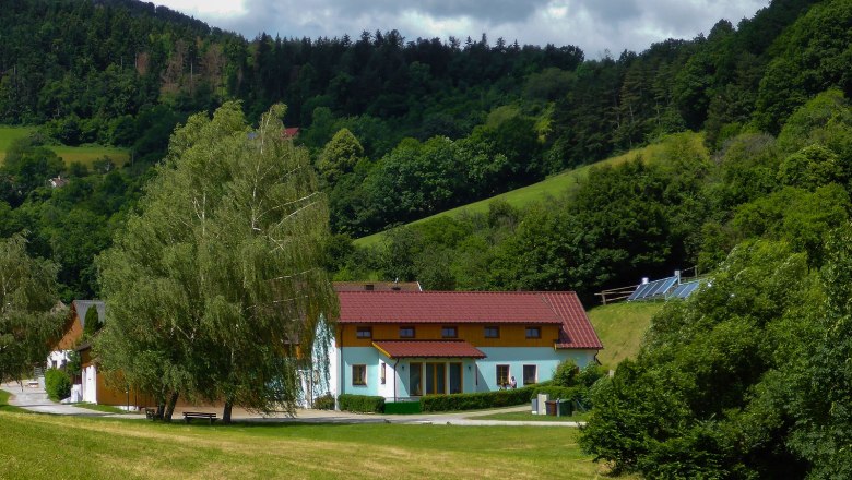 Ferienhof Gruber, © Gruber Claudia Ein Ferienhof mit roten Dächern in einer grünen, hügeligen Landschaft mit Bäumen und Wiesen.