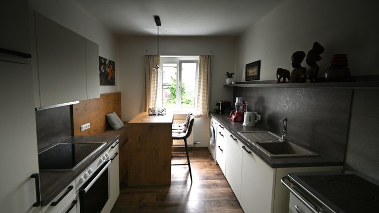 Moderne K&uuml;che mit Holz- und Metallakzenten, Esstisch am Fenster, K&uuml;chenger&auml;te und Dekorationen auf Regalen.