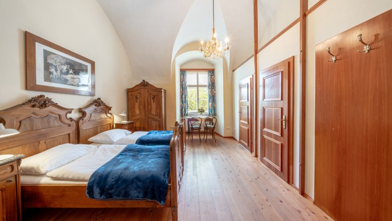 StiftAltenburg_Doppelzimmer, © Martin Mathes Ein elegantes Doppelzimmer mit antiken Holzmöbeln, einem Kronleuchter und einem Fenster mit Blick ins Grüne.