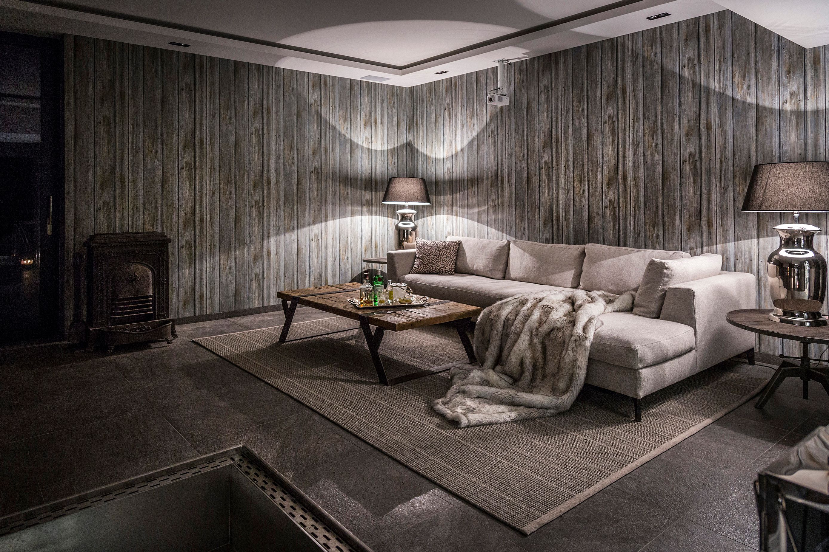 Gemütlicher Raum mit grauem Sofa, Holztisch, Kamin und Holzvertäfelung.