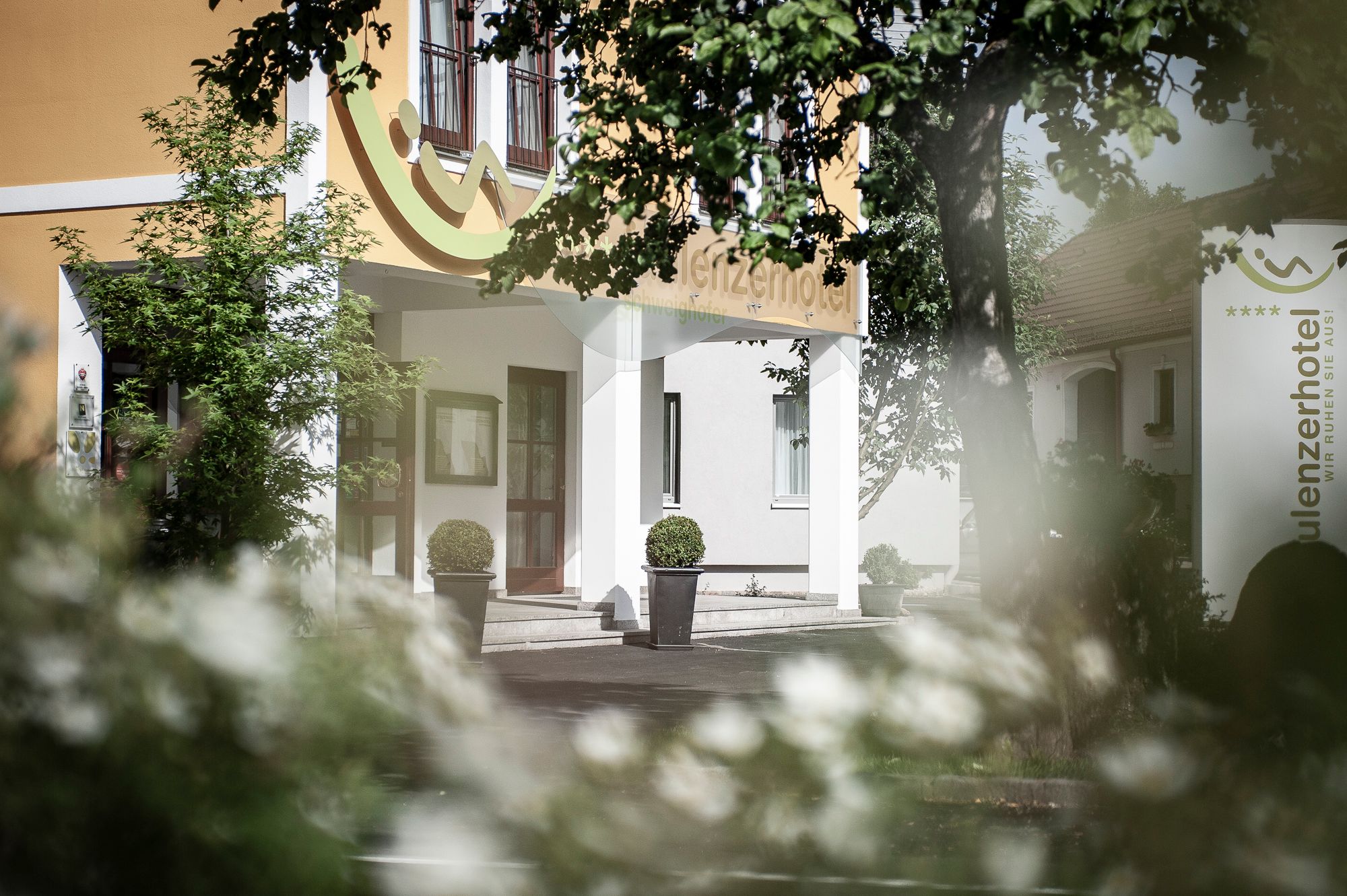 Eingang des Faulenzerhotels mit Pflanzen und Bäumen im Vordergrund.