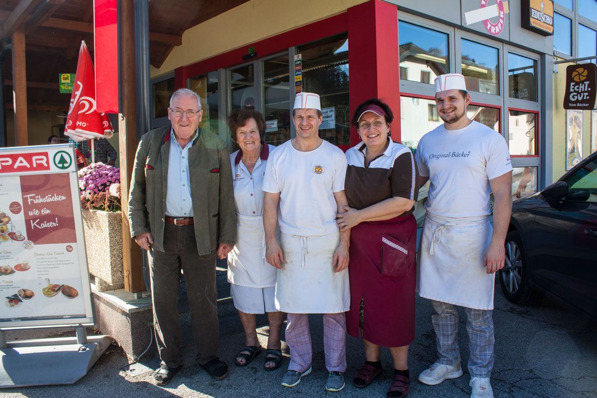 Fünf Personen stehen lächelnd vor einem Geschäftseingang.