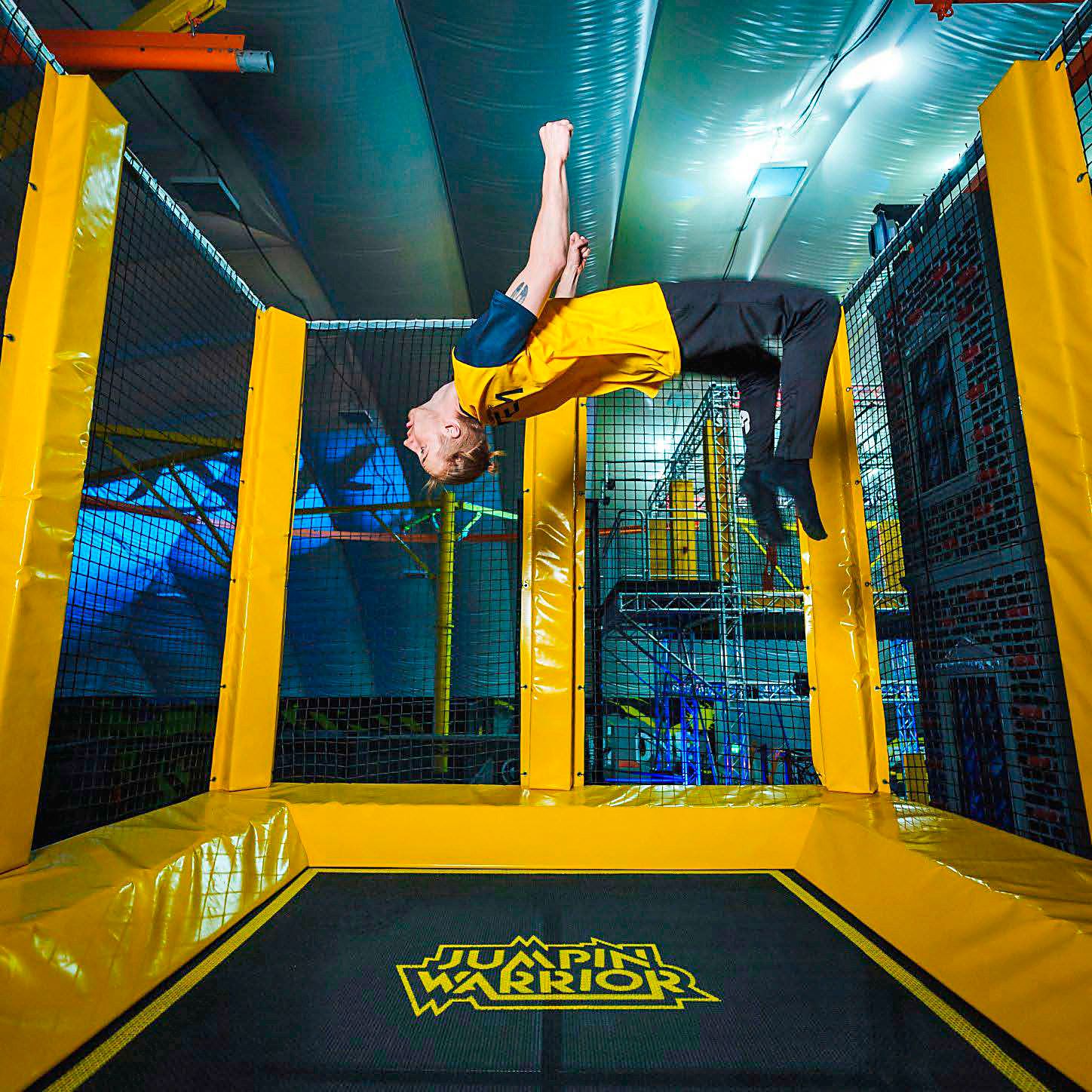 Person macht einen Rückwärtssalto auf einem Trampolin in einer Halle.