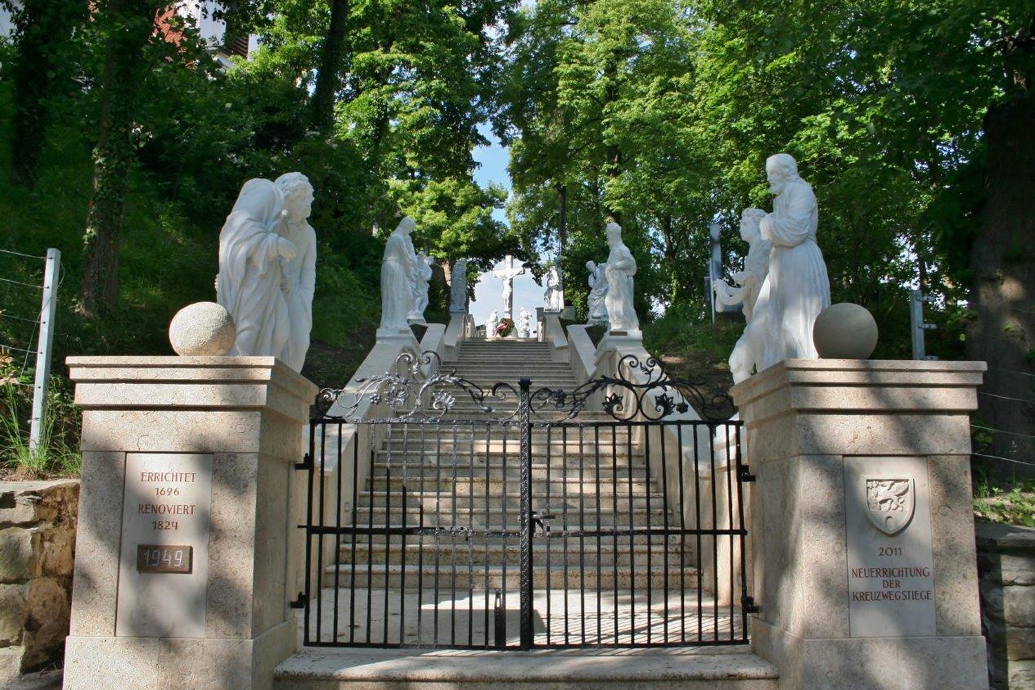 Steintreppe mit weißen Statuen und einem schmiedeeisernen Tor.