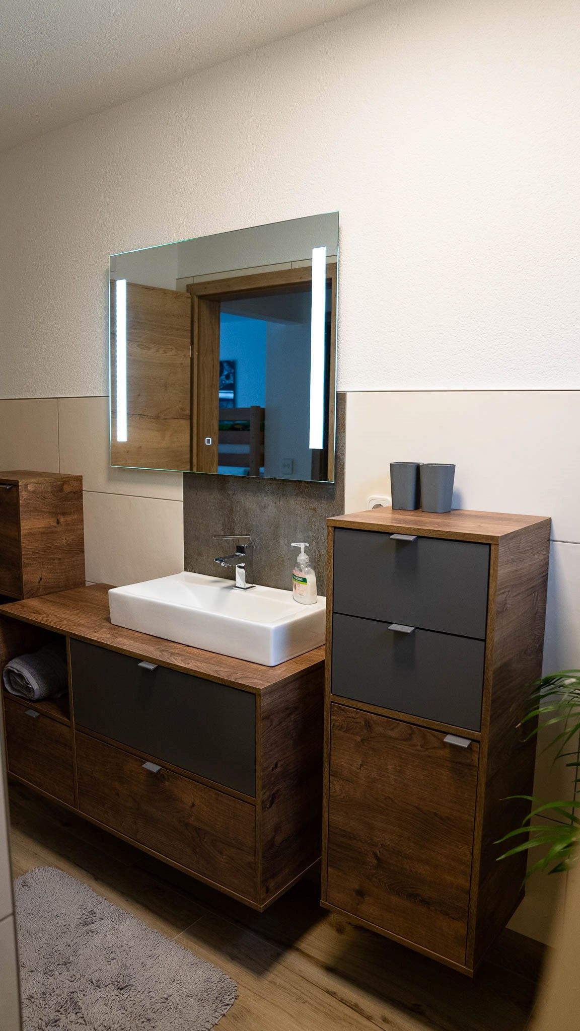 Modernes Badezimmer mit Holzschränken, Waschbecken und beleuchtetem Spiegel.