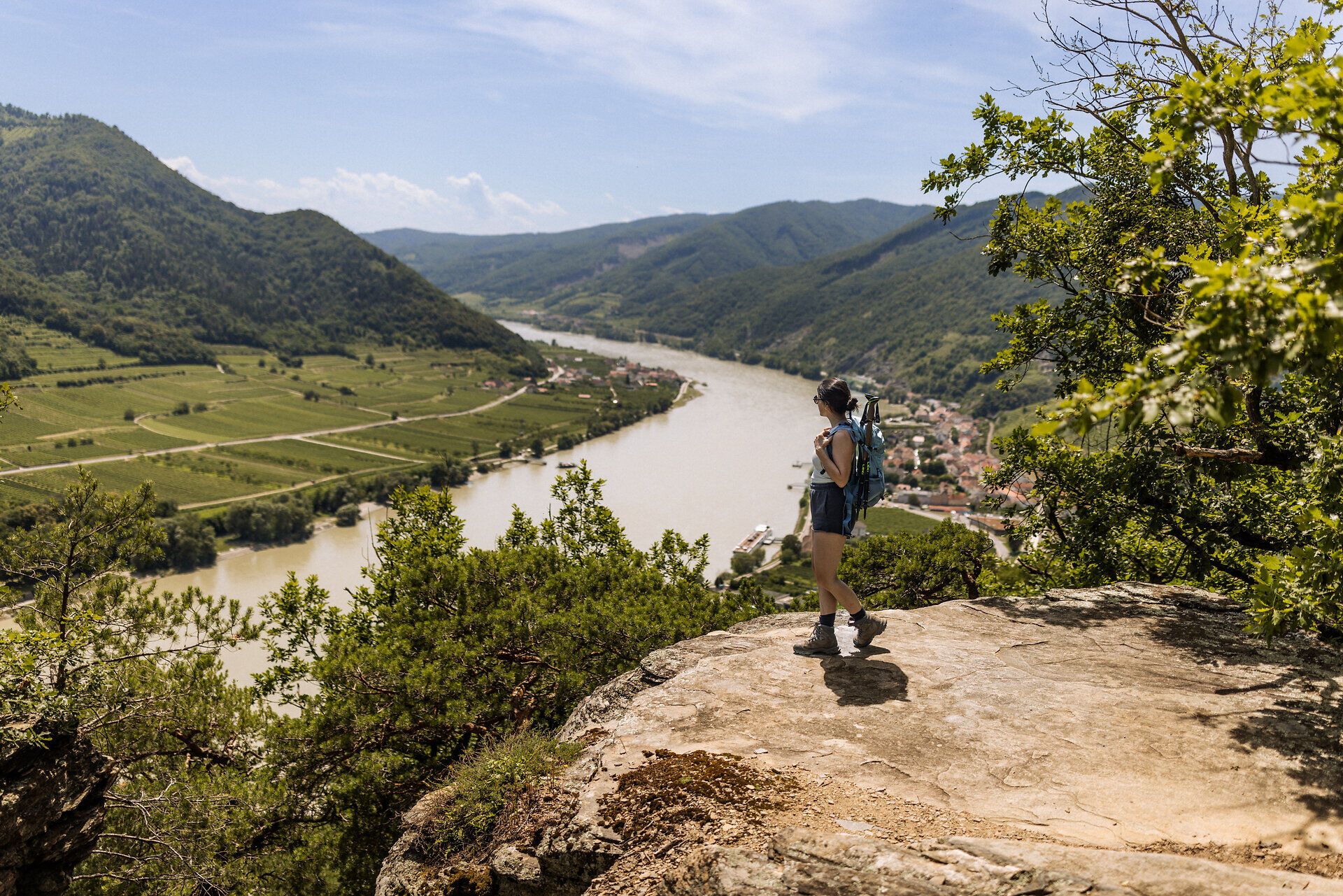 Eine Frau steht auf einem Felsen mit dem Donautal auf Höhe von Spitz an der Donau im Hintergrund.