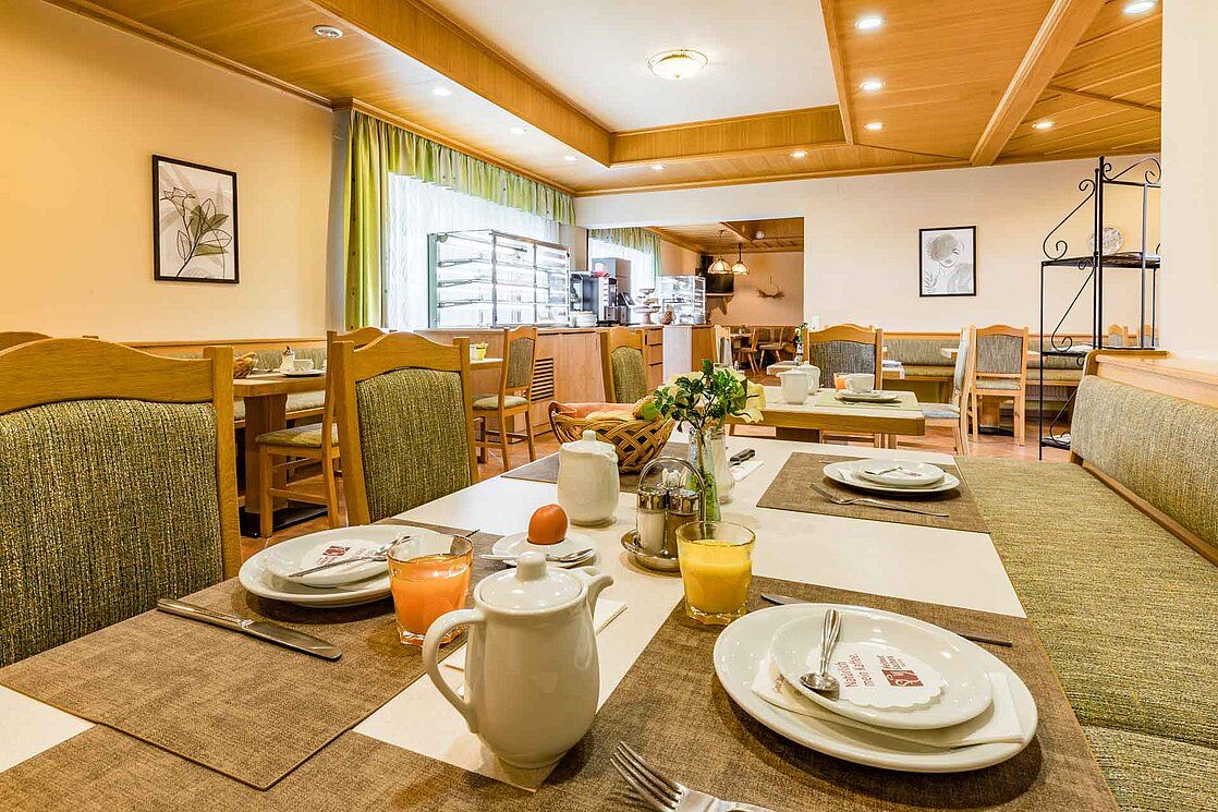 Ein gemütlicher Frühstücksraum mit gedeckten Tischen, Saftgläsern und Kaffeekannen.