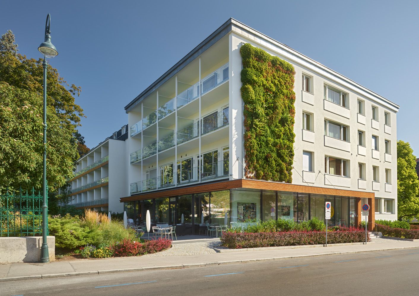 Moderne Gebäudeaußenansicht mit vertikalem Garten und Glasbalkonen bei Tageslicht.