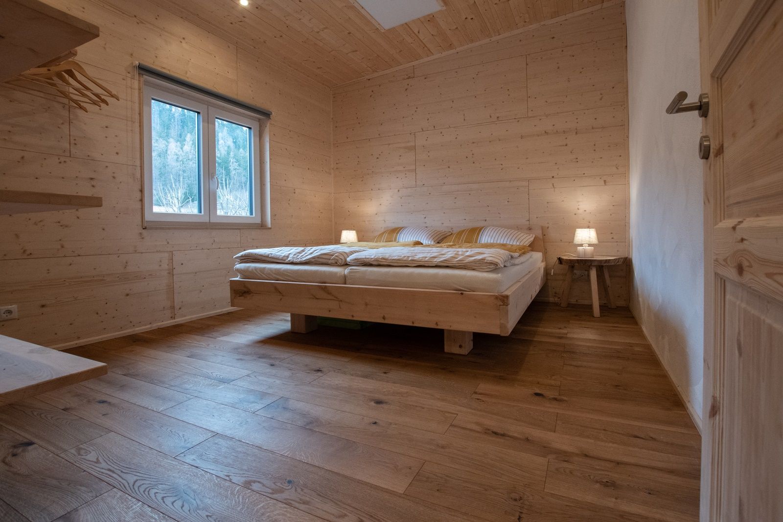Holzverkleidetes Schlafzimmer mit Doppelbett und Nachttischlampen.
