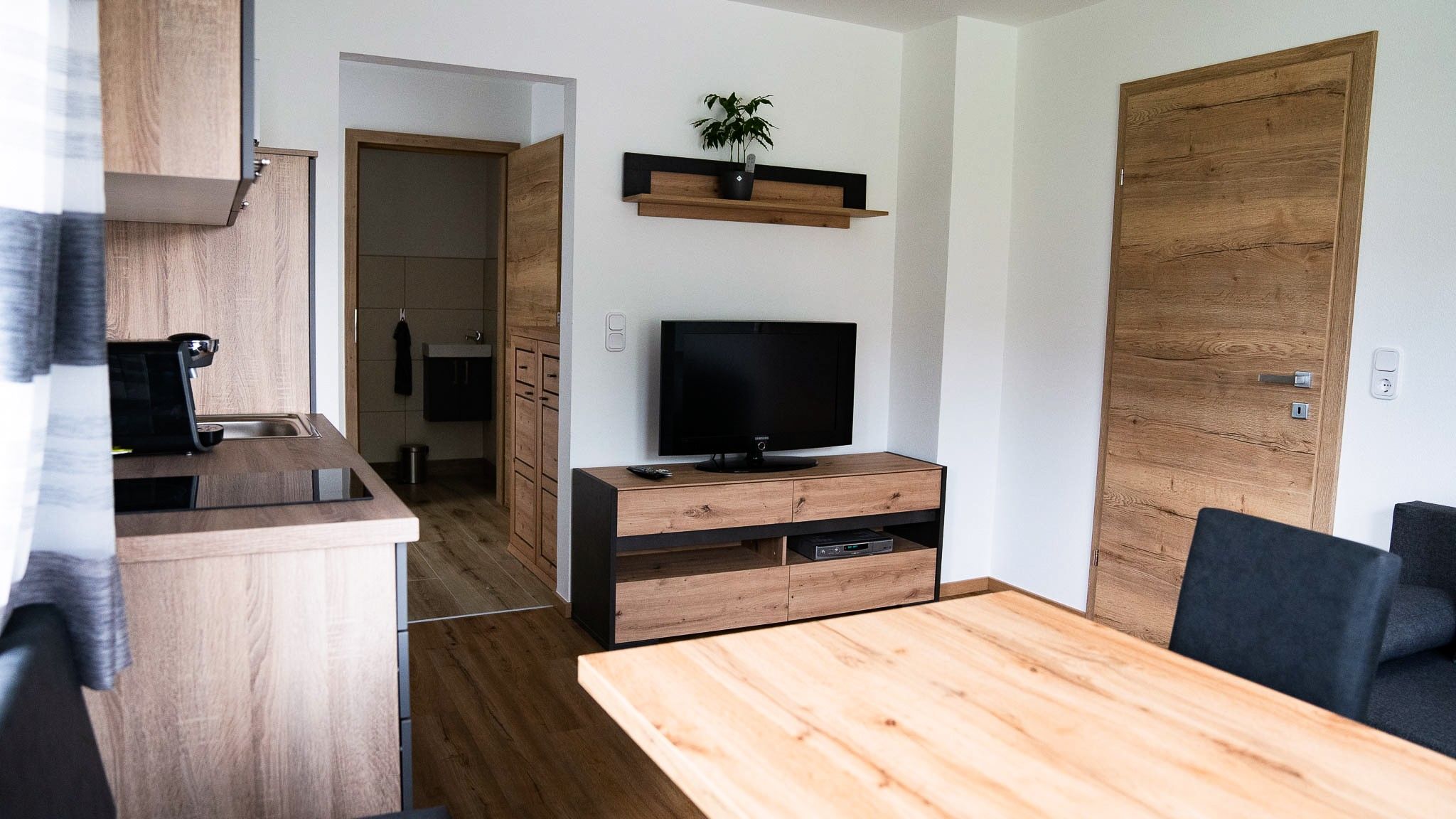 Modernes Wohnzimmer mit Holzmöbeln, Fernseher und Küche.