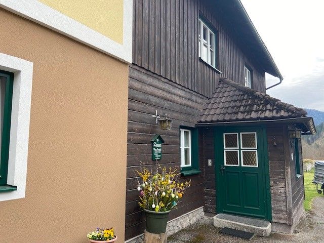 Eingang eines traditionellen Hauses mit Holzverkleidung und grünem Türrahmen.