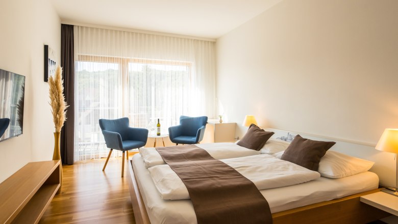Modernes G&auml;stezimmer mit Doppelbett, blauen Sesseln und gro&szlig;en Fenstern.