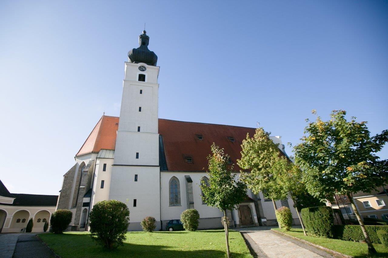Wallfahrtskirche Mank mit Turm und rotem Dach, umgeben von Bäumen und Rasenfläche.