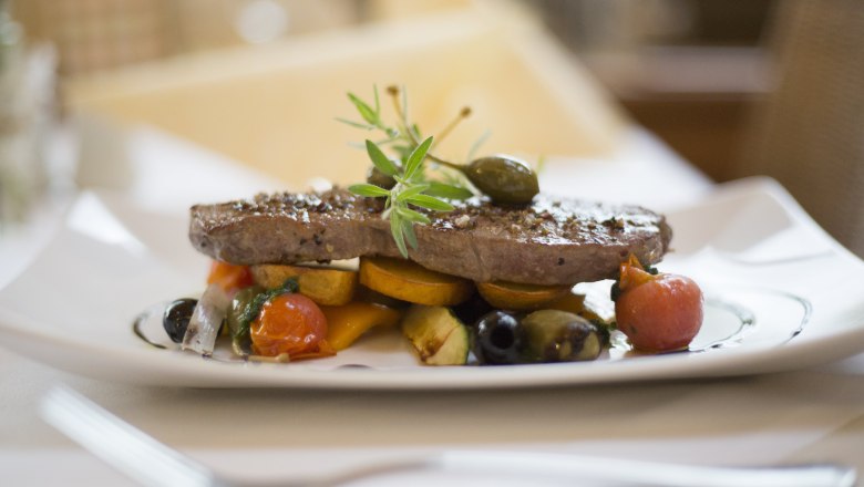 Ein Teller mit einem Stück Fleisch, garniert mit Gemüse und Kräutern.