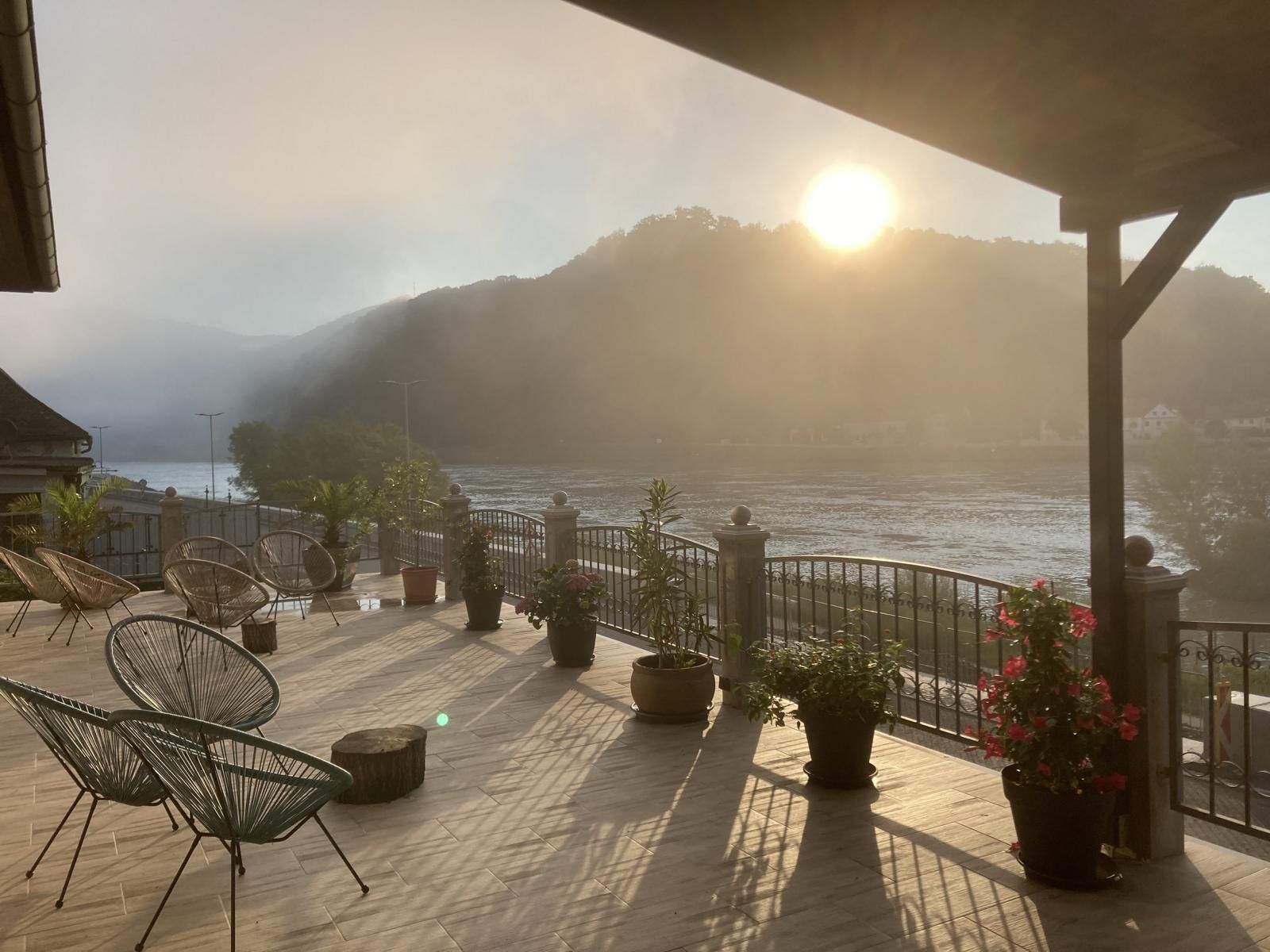 Terrasse mit Blick auf Fluss und Berge im Sonnenaufgang.