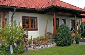 Ein Haus mit rotem Ziegeldach, umgeben von einem Garten mit Kakteen und Str&auml;uchern.