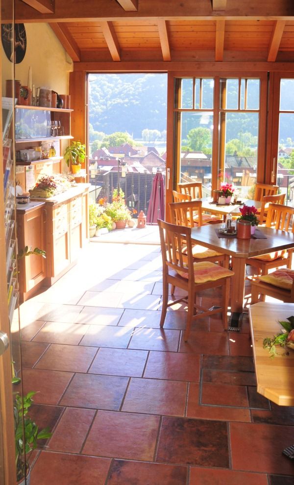 Innenraum eines sonnigen Wintergartens mit Holzmöbeln und Blick auf eine Landschaft.