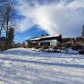 Winterlandschaft mit einem Haus im Schnee, umgeben von B&auml;umen und blauem Himmel.