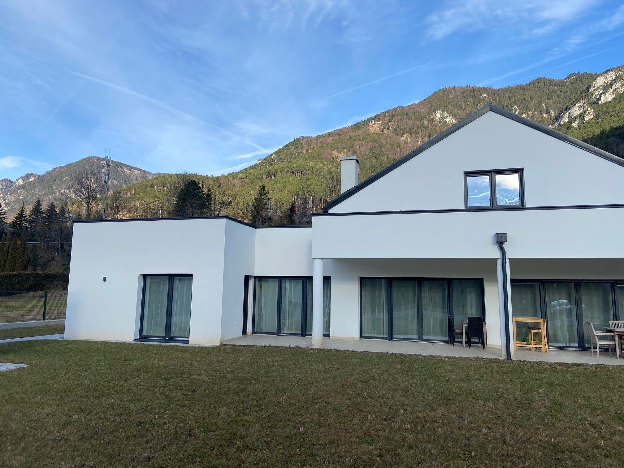 Modernes weißes Haus mit großen Fenstern vor einer Bergkulisse.