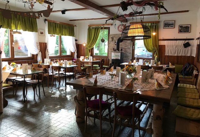 Gemütlicher Gastraum mit Holzmöbeln, dekoriert mit Blumen und Tischdecken.