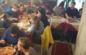 Gruppe von Menschen isst Pizza in einem gemütlichen Restaurant mit Höhlenwänden.