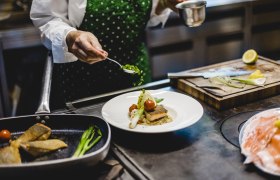 Koch dekoriert ein Gericht mit Kr&auml;utern in einer K&uuml;che.