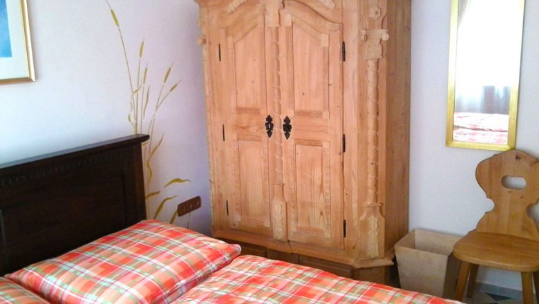 Gästezimmer mit Holzmöbeln und kariertem Bettbezug.