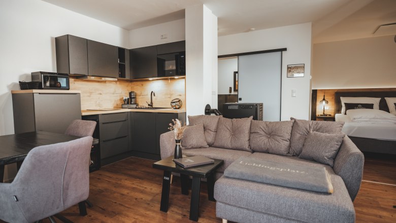 Moderner Wohnbereich mit grauem Sofa, K&uuml;chenzeile und Esstisch.