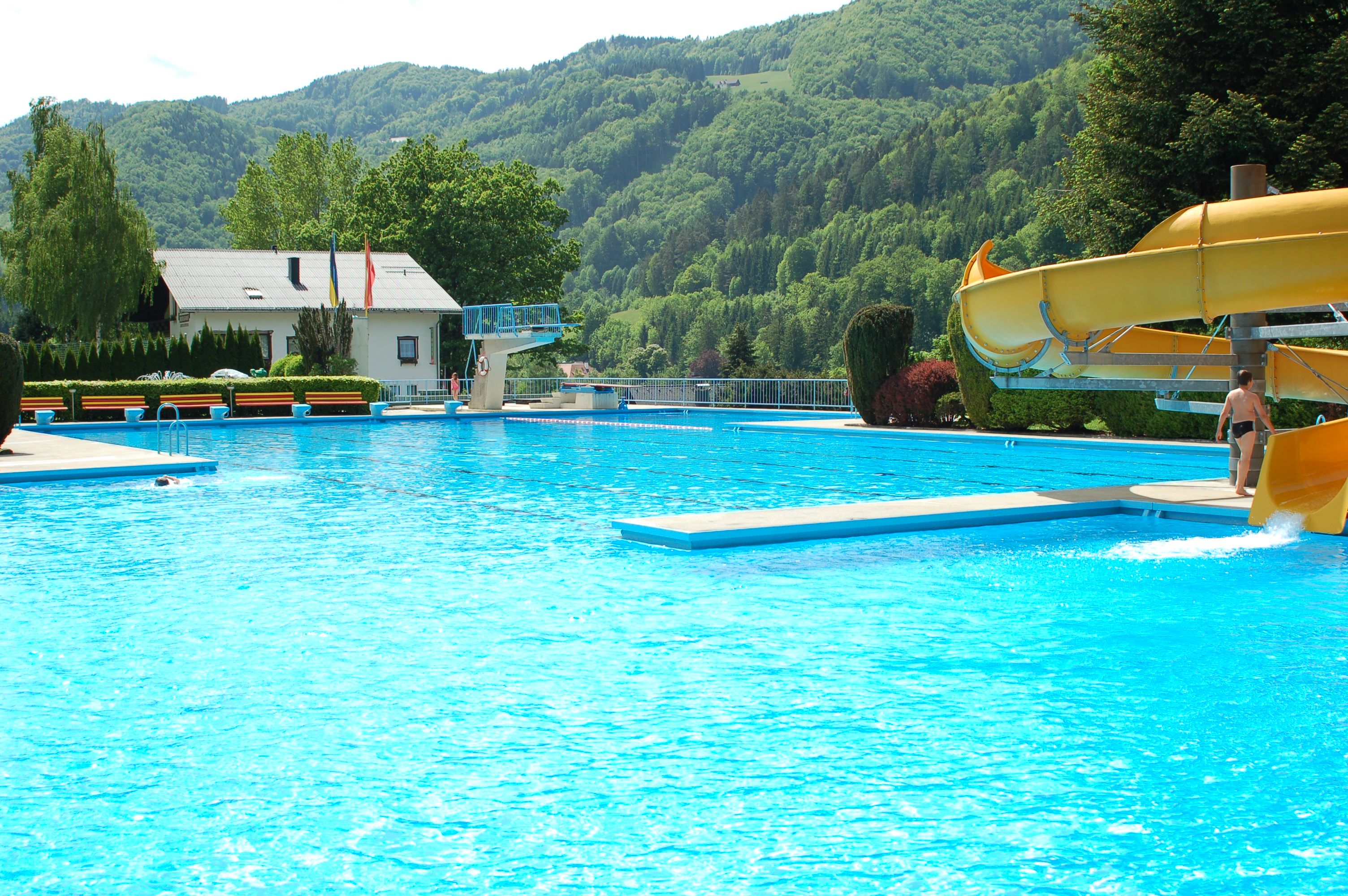Ein Freibad mit Rutsche, Sprungbrett und umliegenden Bergen.