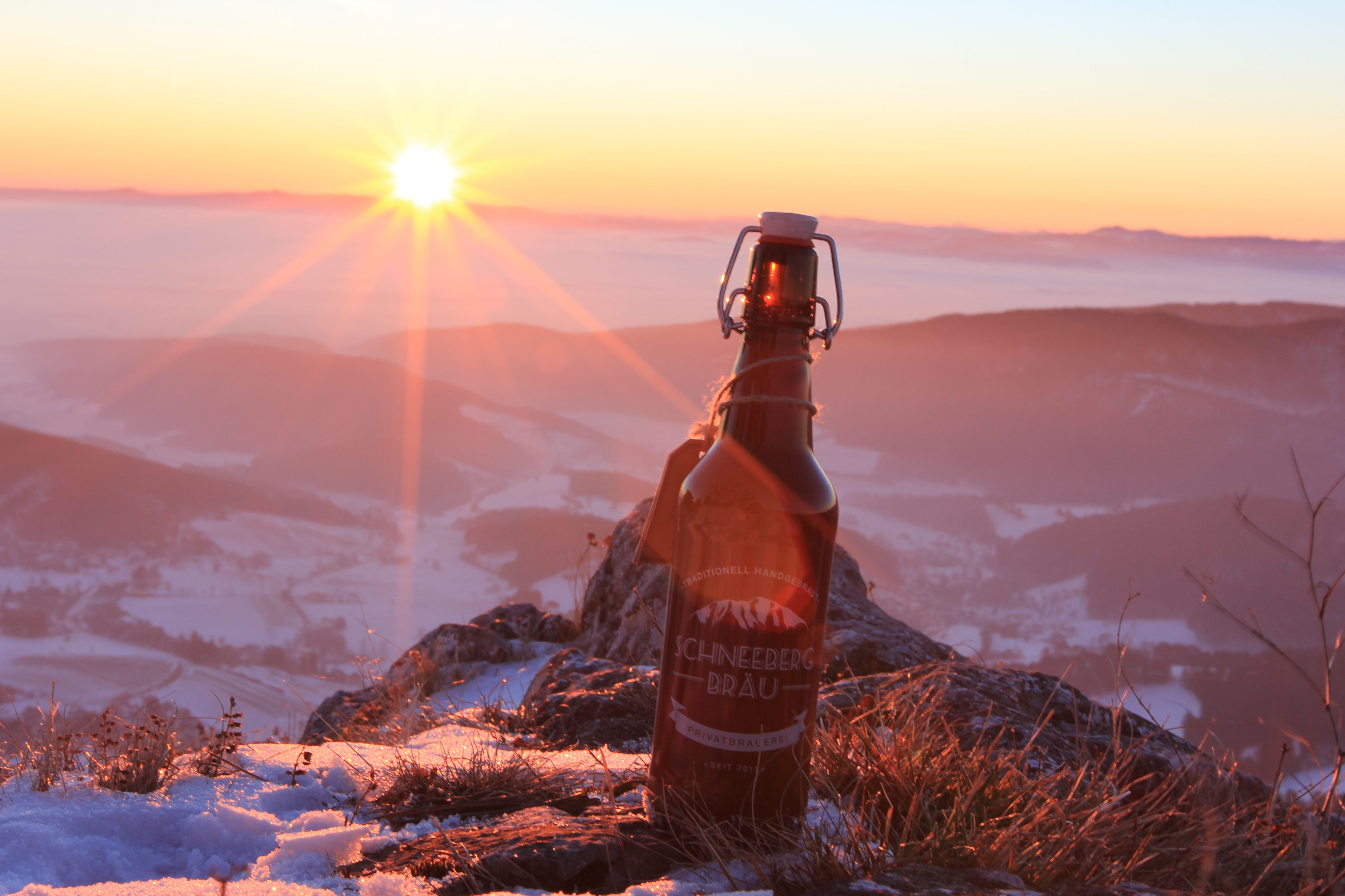Eine Flasche Schneeberg Bräu Bier steht auf einem schneebedeckten Berg bei Sonnenuntergang.