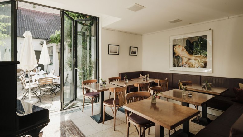 Gemütliches Gastzimmer mit Holztischen, Kunst an der Wand und Terrasse im Freien.
