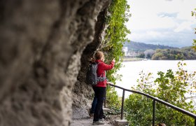 Zwei Frauen auf einem Wanderweg blicken aufs Wasser. Im Hintergrund Felsen.