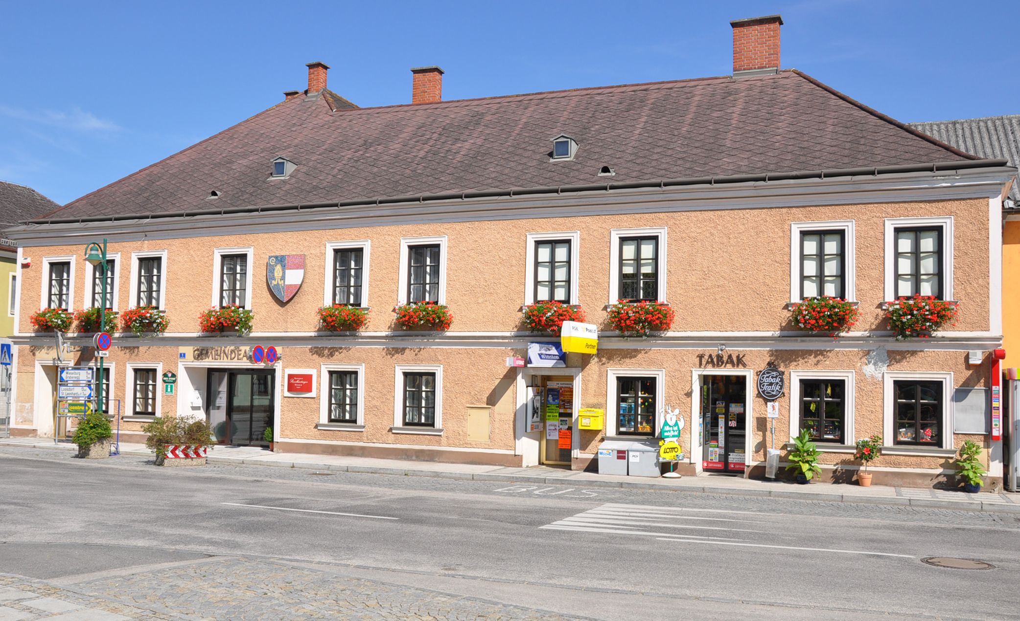 Ein zweistöckiges Gebäude mit Blumen an den Fenstern und Geschäften im Erdgeschoss in Ruprechtshofen.