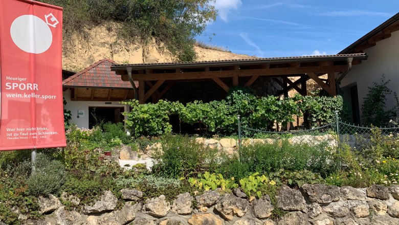 Außenansicht eines Heurigen mit Garten und Werbeschild.