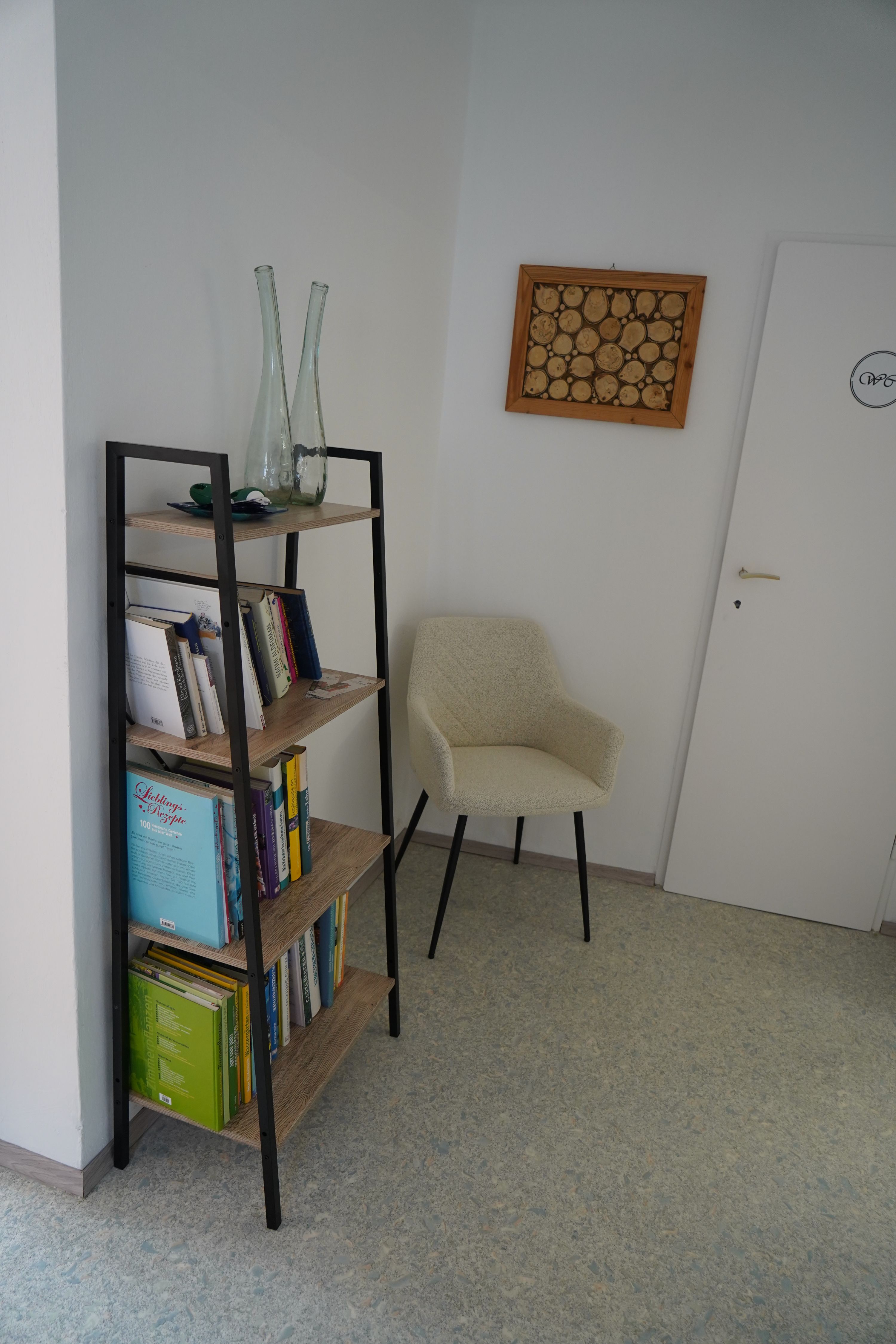 Ein Bücherregal mit Büchern und Dekoration, daneben ein beiger Stuhl und eine Tür in einem Raum.