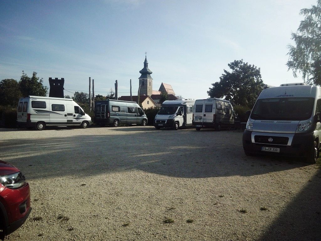 Wohnmobilstellplatz mit mehreren geparkten Wohnmobilen und einer Kirche im Hintergrund.
