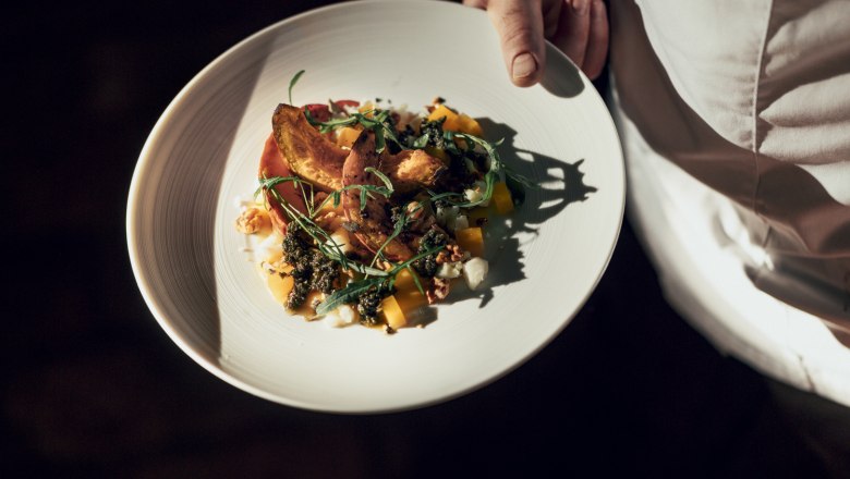 Ein Teller mit geröstetem Hokkaido-Kürbis, Salbeipesto und Schafkäse, gehalten von einer Person in weißer Kleidung.