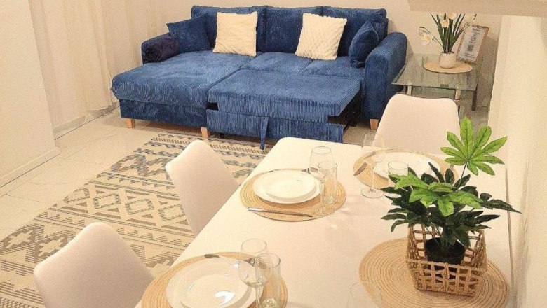 Wohnzimmer mit blauem Sofa und Esstisch mit Gedeck.