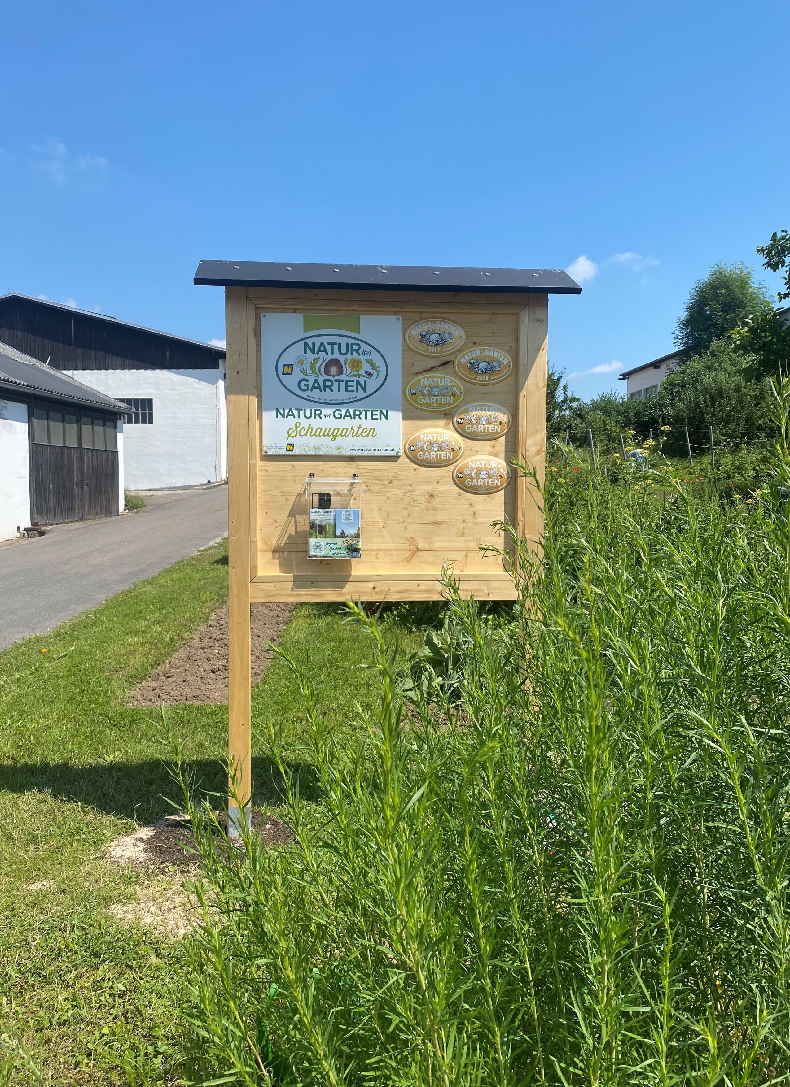 Holztafel mit Natur im Garten Schaugarten-Logo und Plaketten, umgeben von Pflanzen.