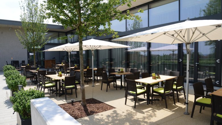 Terrasse eines Restaurants mit Tischen, St&uuml;hlen und Sonnenschirmen.