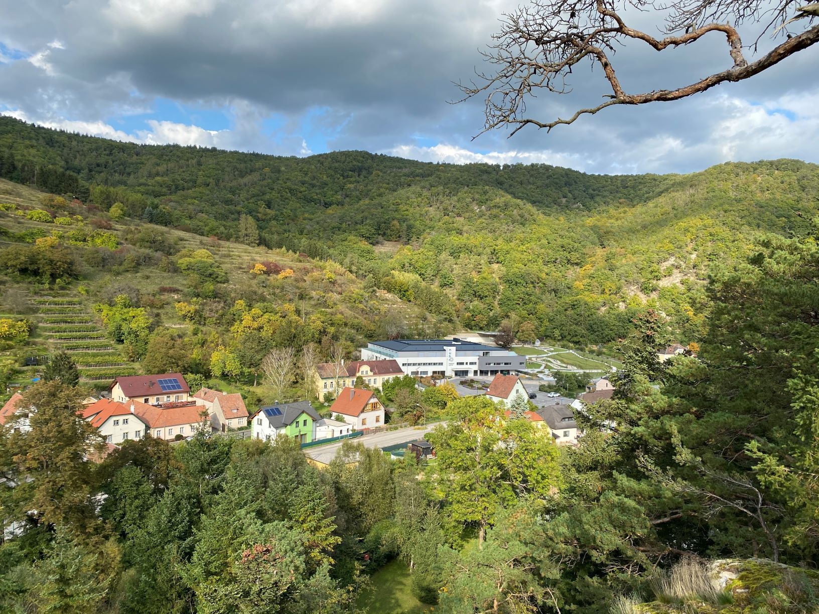 Blick vom Joschi-Felsen auf ein Dorf mit Häusern und bewaldeten Hügeln im Hintergrund.
