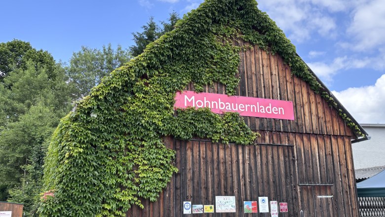 Holzgeb&auml;ude mit Efeu bewachsen, Schild 'Mohnbauernladen'.