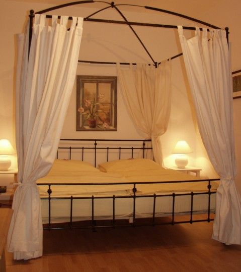 Ein Himmelbett mit weißen Vorhängen in einem gemütlichen Schlafzimmer, beleuchtet von zwei Nachttischlampen.