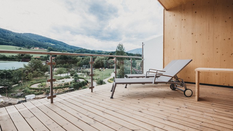 Holzterrasse mit Liegestuhl und Blick auf gr&uuml;ne Landschaft und Berge.