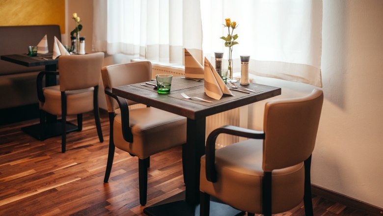 Gem&uuml;tliches Restaurant mit Holzboden, gedecktem Tisch und Blumen.