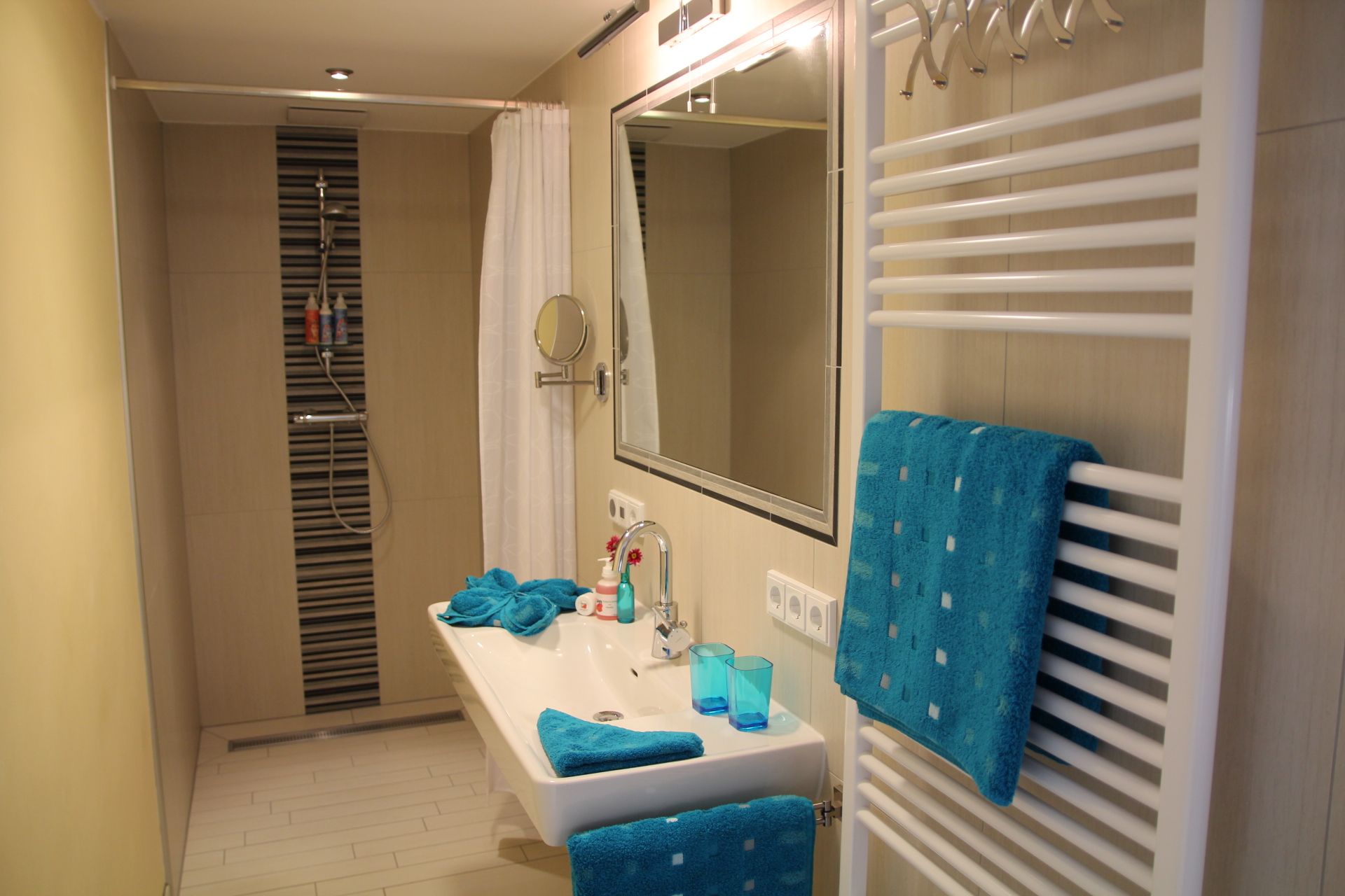 Modernes Badezimmer mit Dusche, Waschbecken und blauen Handtüchern.