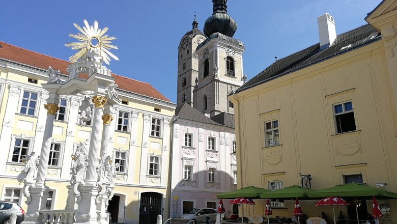 Historischer Platz mit barocker Säule, Kirche und Café.